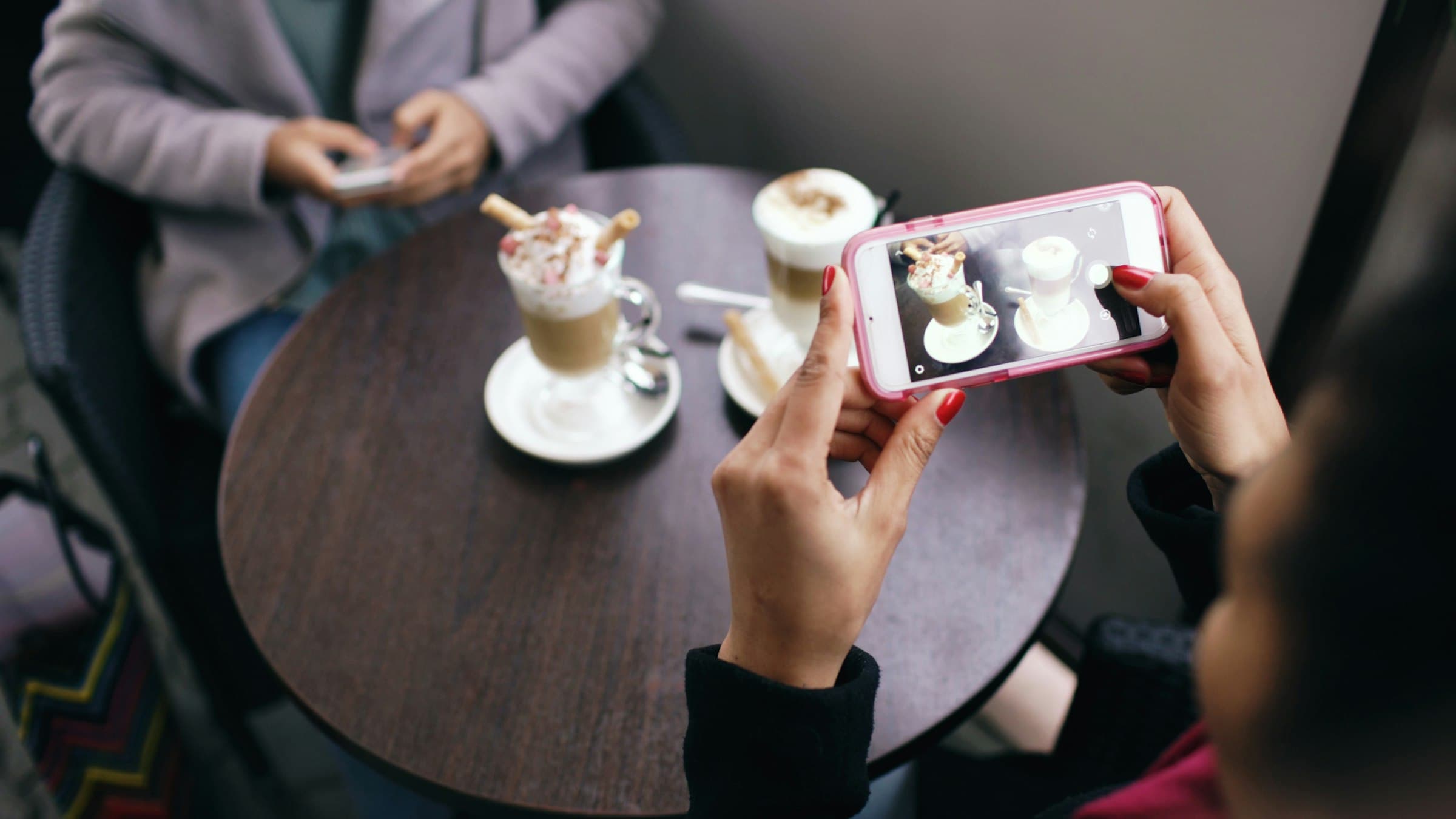 Guest holding a phone over a cafe table with two coffee drinks
